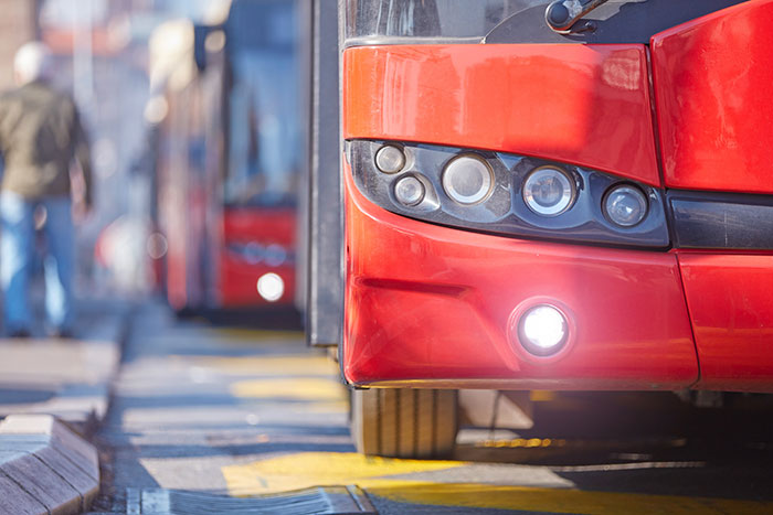 Close-up of a red bus on a city street with a blurred background of pedestrians and other buses. - 2