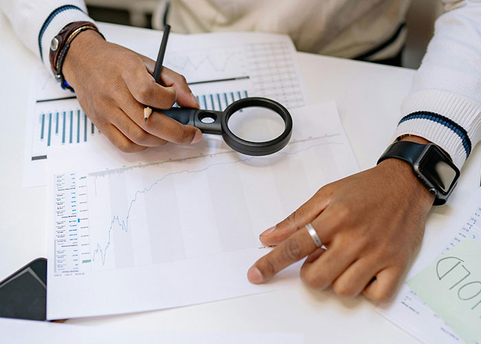Person analyzing charts with a magnifying glass and pencil, representing jobs that only a person without a soul would do