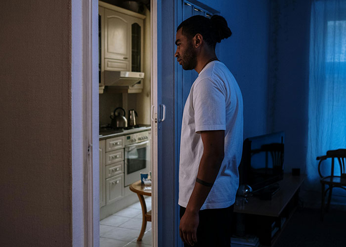Young man in a white shirt standing by a doorway at night, reflecting on wild and embarrassing drinking stories.