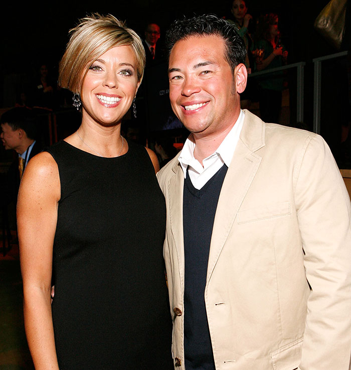 Kate and Jon Gosselin smiling at a social event with people in the background, dressed in formal attire.