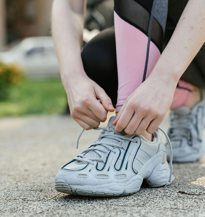 Person wearing running clothes tying shoelaces outdoors, related to cops wearing running clothes to elicit catcalls.