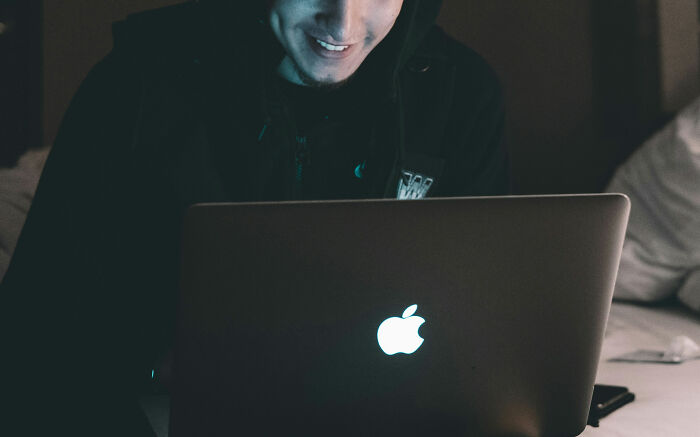 Person smiling while using a laptop in a dimly lit room, illustrating Reddit not for the faint of heart moments.