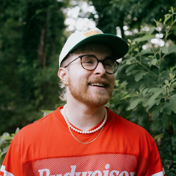 Young man wearing glasses and a cap smiling outdoors, representing short king and debates on height preferences in dating.