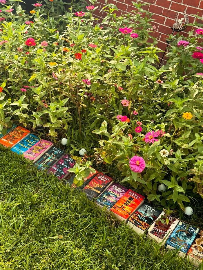 Colorful garden decor pieces made homes more magical with vibrant flowers lining a brick wall in a lush green yard.