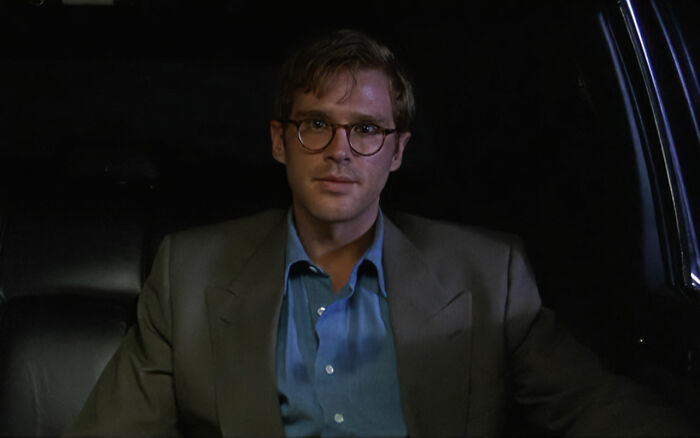 Man wearing glasses and a gray blazer sitting in a car, related to Alicia Silverstone kissing her co-star at age 15. Man wearing glasses and a gray blazer sitting in a car, related to Alicia Silverstone kissing her co-star at age 15.