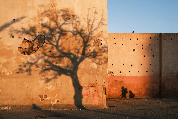Shadow of a tree and two people cast on worn walls during a candid everyday moment in Asia by photographer Gil Kreslavsky