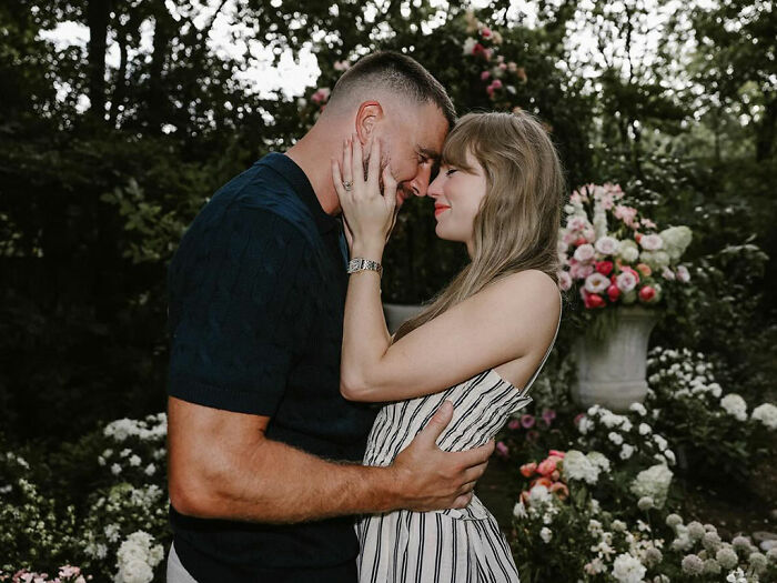 Couple embracing warmly outdoors, with floral arrangements in the background, highlighting Taylor Swift's engagement marketing stunt debate.