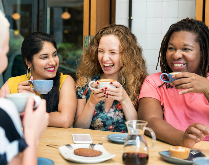 Group of diverse friends drinking coffee and laughing together showcasing things Americans do that make them stand out abroad