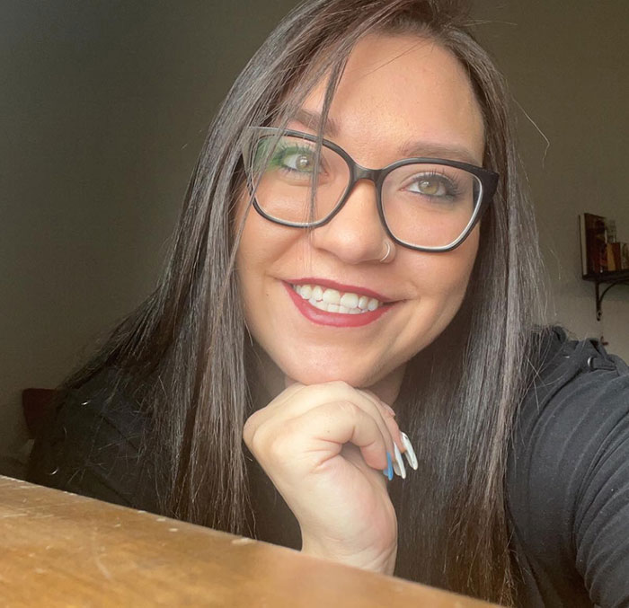 Young woman with glasses smiling indoors, representing family awarded nearly a billion dollars after gravely disabled baby case.