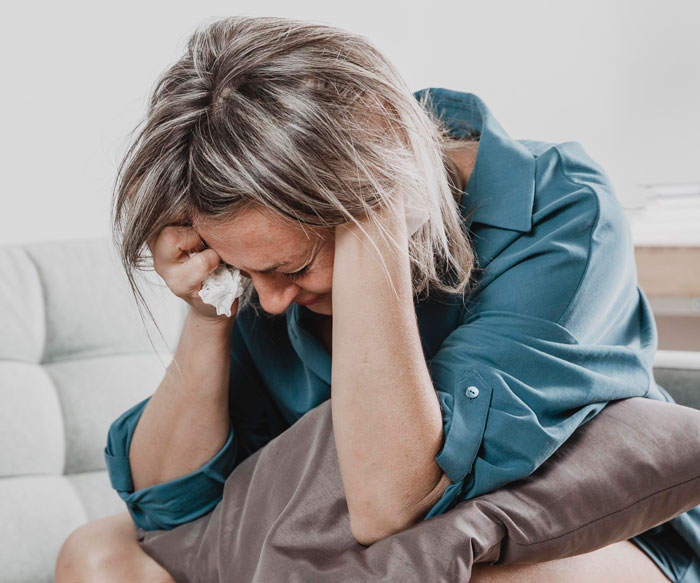 Woman in a blue shirt holding a pillow and tissue, appearing distressed after influencer neighbors put woman hospital incident Woman in a blue shirt holding a pillow and tissue, appearing distressed after influencer neighbors put woman hospital incident