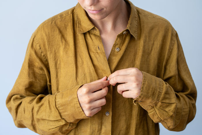 Woman buttoning shirt, symbolizing frustration and reflection related to sexism and job challenges.