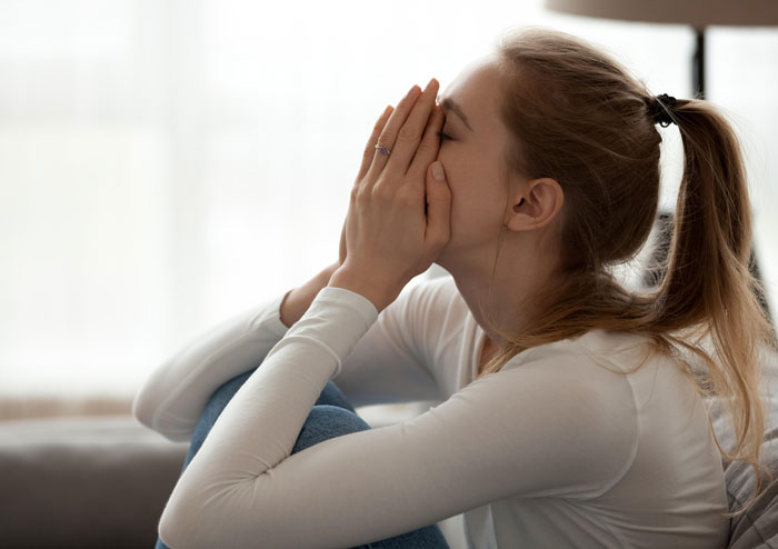 Woman sitting indoors, covering her face with hands, appearing distressed after dog attacks stalker at her home. Woman sitting indoors, covering her face with hands, appearing distressed after dog attacks stalker at her home.