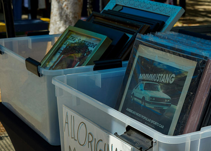 Vintage car posters in plastic bins displayed outdoors, featuring classic Mustang and other automotive images.