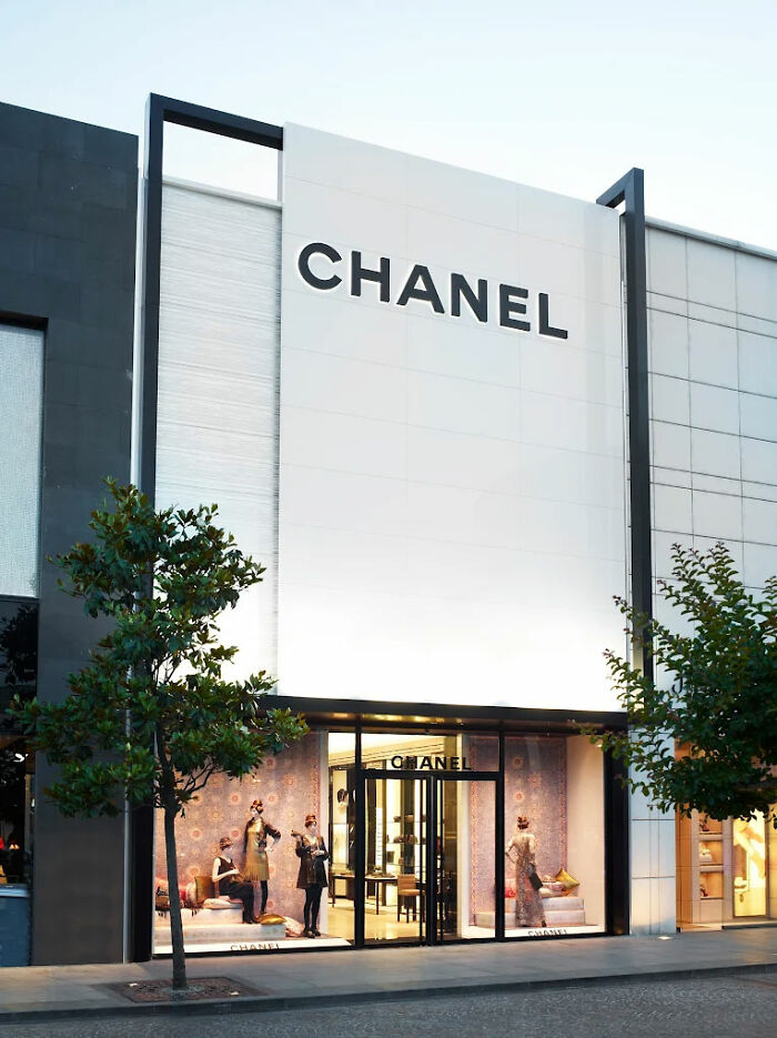 Chanel store exterior with mannequins in window display and trees lining the sidewalk at dusk.