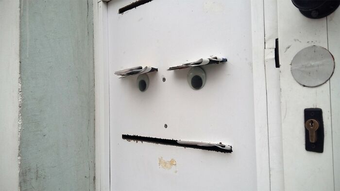 White door with two googly eyes and newspaper pieces resembling street art creating a face-like expression.