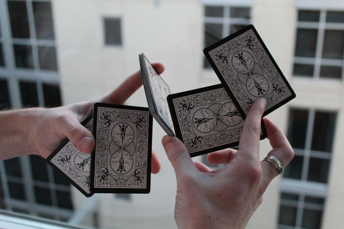 Hands smoothly fanning playing cards against a blurred city window, illustrating smooth pickup lines in action.