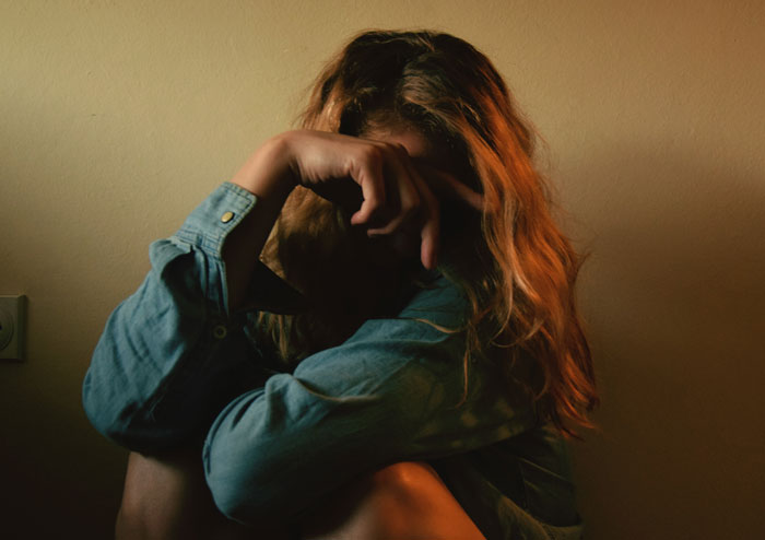 Woman sitting alone in dim light, covering face with arm, reflecting emotions related to sexism and job challenges.