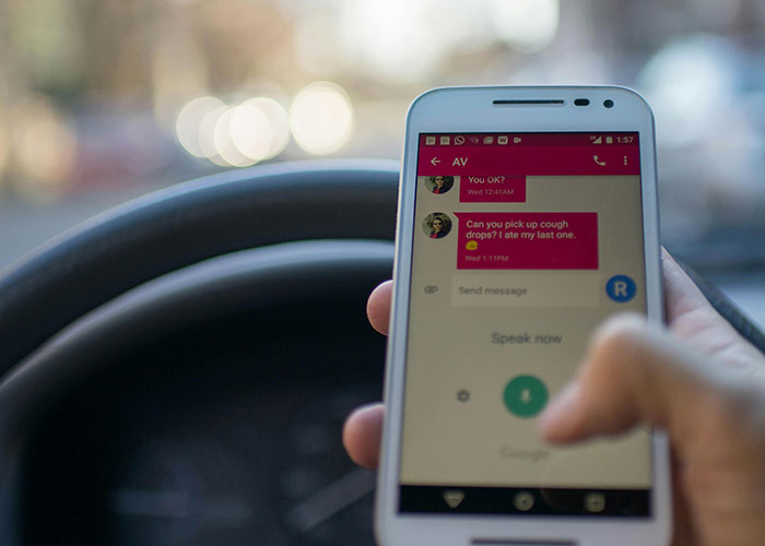 Person using a smartphone while driving, illustrating common illegal actions such as speeding and distracted driving.