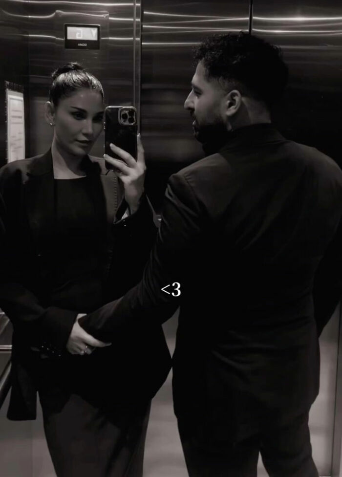 Couple dressed in black taking a mirror selfie in an elevator, related to intoxicated man’s threat and supermodel wife defense. Couple dressed in black taking a mirror selfie in an elevator, related to intoxicated man’s threat and supermodel wife defense.