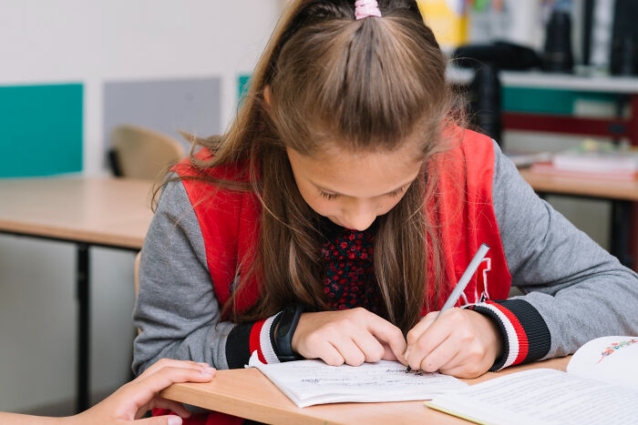 School kid confidently writing in a notebook at desk, demonstrating focus and determination in a classroom setting