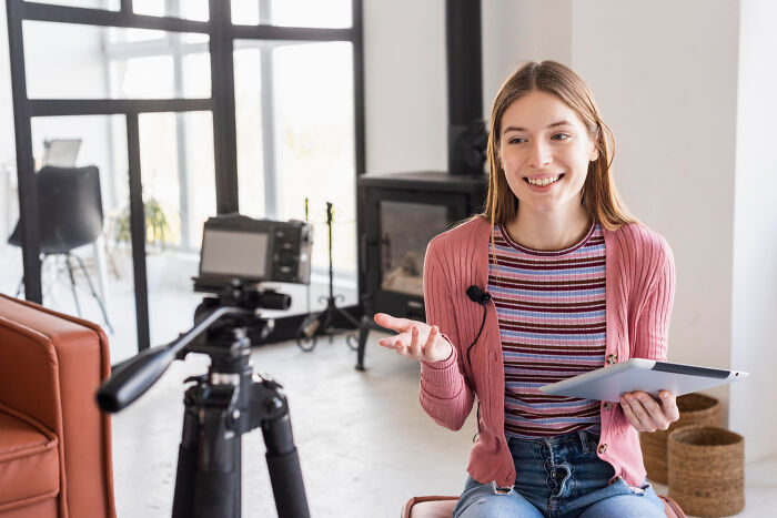 Young woman sharing unhinged hacks to land job, holding tablet and speaking to camera in a bright home studio.
