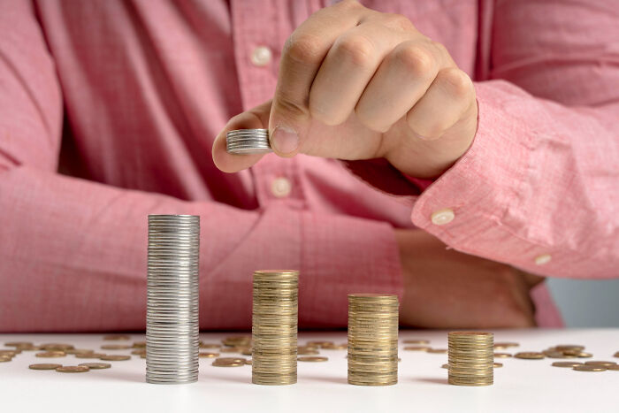 Person stacking coins in ascending order on table, illustrating low effort high reward concept with money growth.