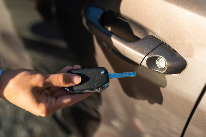 Hand holding a car key close to a car door handle, illustrating employees skipping work for unusual reasons.