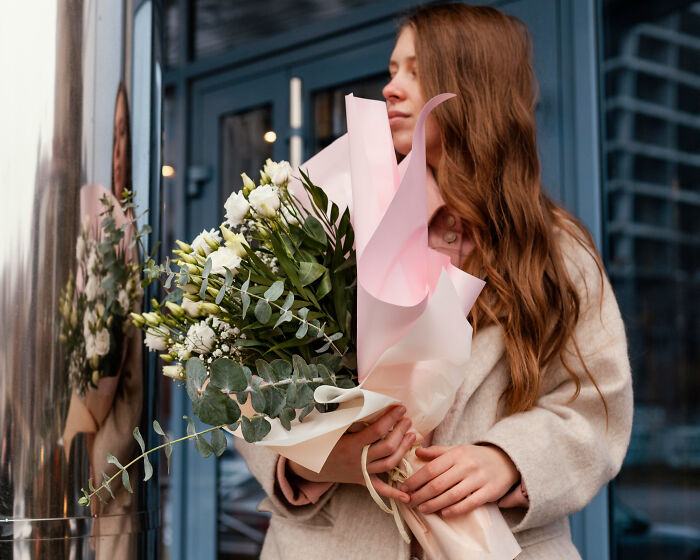 Young woman holding a bouquet of flowers wrapped in pastel paper, showcasing a low effort high reward gesture outdoors.