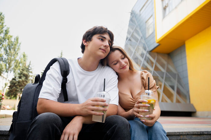 Young couple sitting close, holding drinks outdoors, illustrating smooth pickup lines in a casual setting.