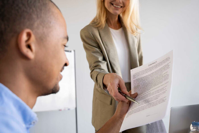 Smiling woman handing contract to man during a job interview showing unhinged hacks done to land job tips.