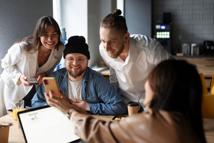 A group of employees laughing and looking at a phone together, illustrating unusual work day skips.