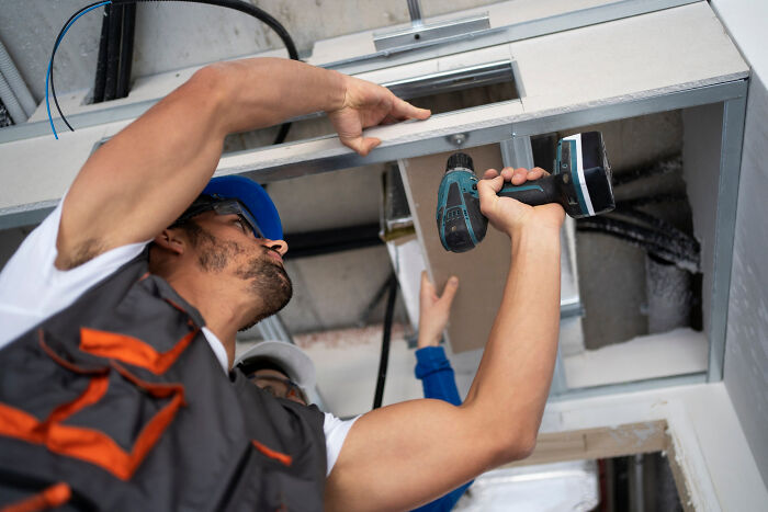 Worker in hard hat using power drill installing ceiling panels, illustrating employees skipping work for unusual reasons.
