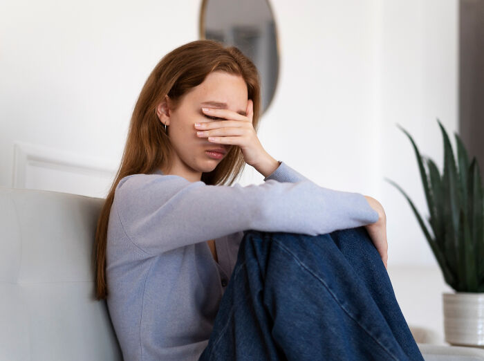A stressed woman sitting on a couch, covering her face, illustrating employees skipping work for insane reasons.