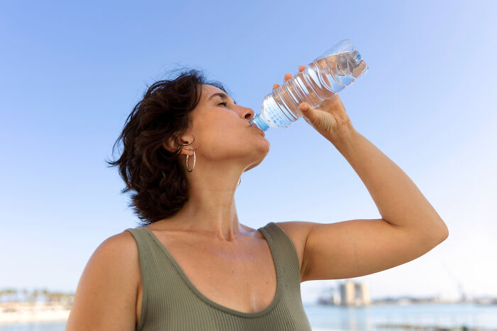 Woman drinking water from a bottle outdoors, illustrating aspects of modern life that may be close to breaking down.