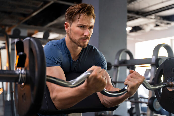 Young man performing low effort high reward weightlifting exercise in gym with focused expression and proper form.