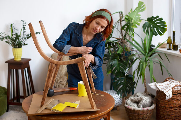 Woman assembling wooden chair at home, demonstrating low effort high reward DIY furniture project ideas.
