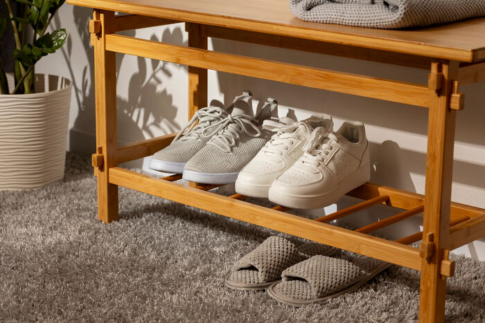 Wooden shoe rack with white and gray sneakers and slippers on a gray carpet, illustrating employees skipping work day.
