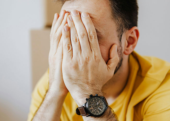 Man in yellow shirt covering his face with hands, showing regret or embarrassment related to wild and embarrassing drinking stories.