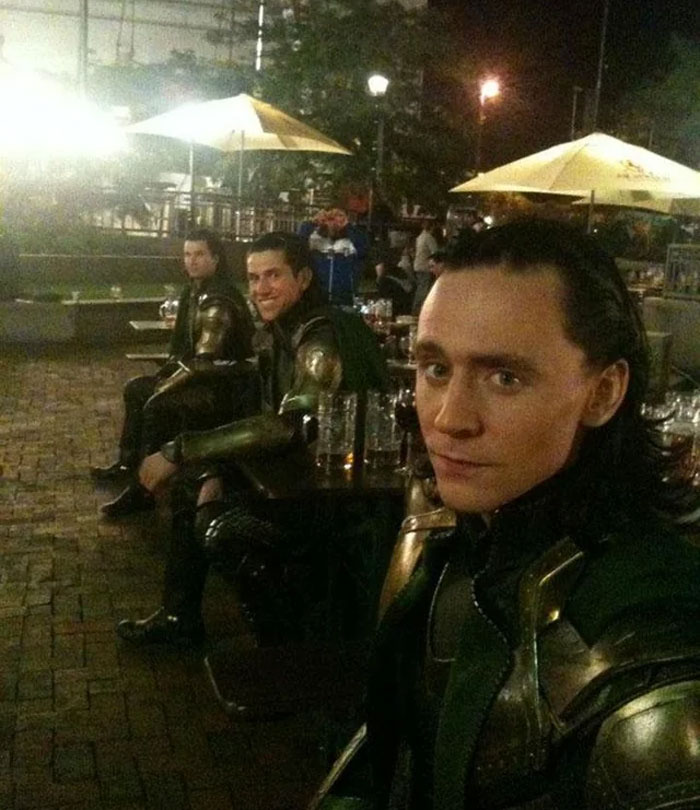 Three men dressed as Loki characters sitting at an outdoor table at night, showcasing insane family flexes.