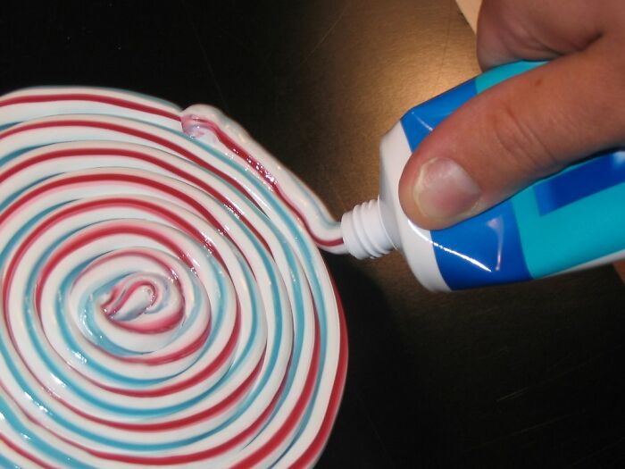 A hand squeezing colorful striped toothpaste in a spiral pattern, symbolizing snooping parents uncovering kids' secrets.