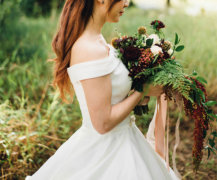Bride in a white wedding dress holding a bouquet outdoors, representing bride tries to cancel guest’s resort room story. - 10