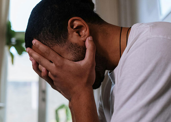 A man covering his face in regret, illustrating the consequences of wild and embarrassing drinking stories.