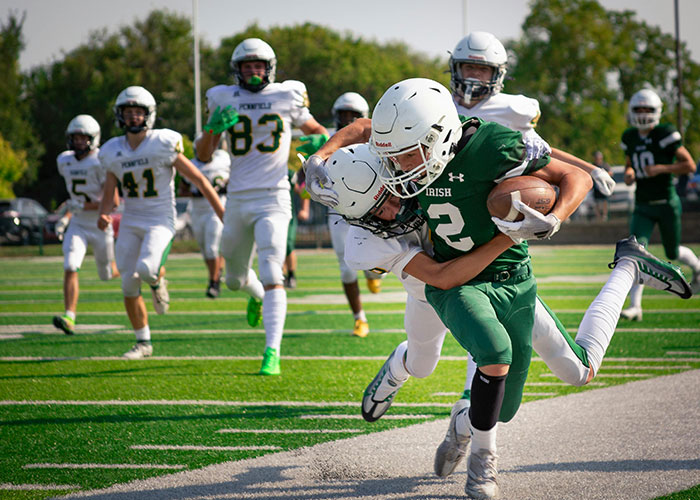 High school football players in action on the field with one tackling another during an intense game moment.