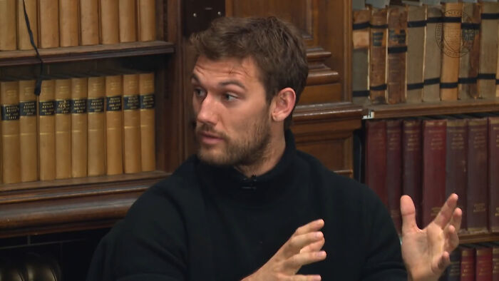 Young male celebrity in black sweater speaking and gesturing during a discussion on Hollywood A-listers and audience reception.