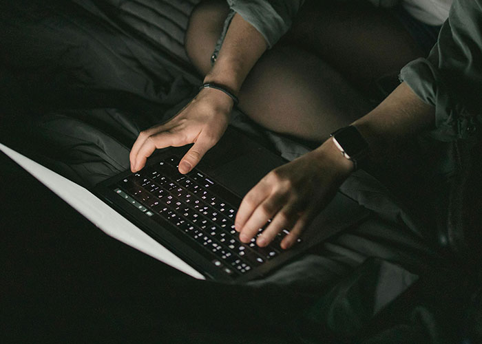 Person typing on a backlit laptop keyboard in a dark room, illustrating the concept of driving over the speed limit.