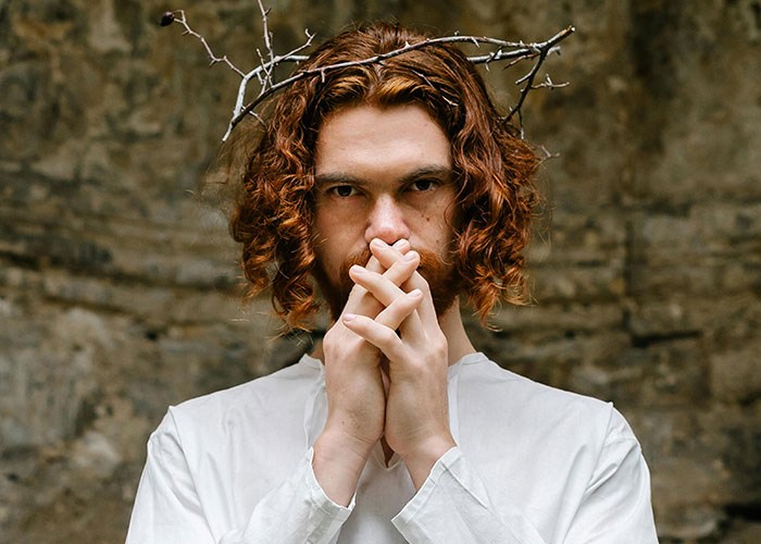 Person with curly red hair wears a crown of thorns and a white shirt, symbolizing jobs for a person without a soul.