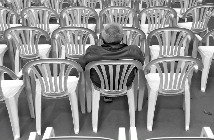 Person seated alone among many empty plastic chairs, capturing one of life’s unseen, unposed moments on the streets.