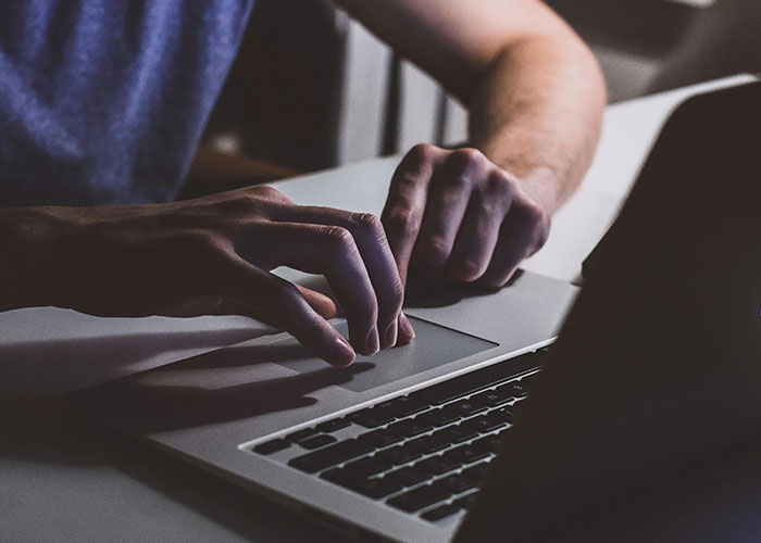 Person using a laptop with hands on the keyboard in a dimly lit room, relating to driving over the speed limit topic.