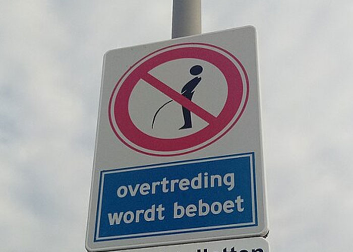 No urinating sign on a pole with a warning in Dutch about fines for illegal actions related to public behavior.