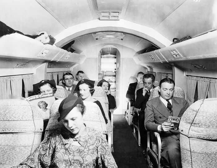 Passengers dressed in glamorous vintage attire inside a classic airplane cabin showcasing flying as an affair of pure glamour.